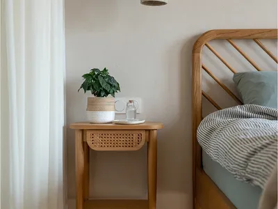 A minimalist bedroom featuring a wooden console table with cane-weave drawers and a potted plant on top.