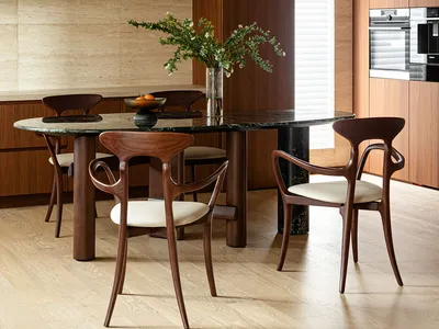 A modern kitchen with an oval dining table, wooden chairs with white upholstery, and a marble countertop. Features include wo