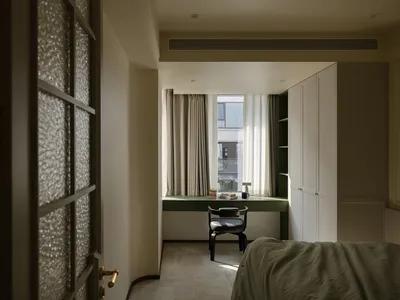 A modern minimalist bedroom featuring a window with curtains, a green desk, black chair, and a bed with a green blanket.