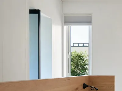 A minimalist bedroom with a wooden headboard and white bedding, featuring a side table with a glass and a newspaper.