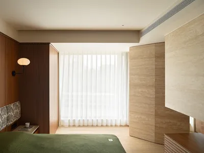 A modern minimalist bedroom with brown wooden finishes and white sheer curtains by the window.