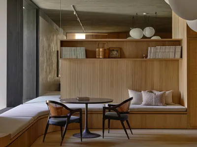 Contemporary wooden lounge area with concrete ceiling, white cushions, and round table and chairs.