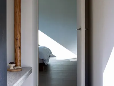 A minimalist bedroom with a white door, wooden floor, and minimal furnishings.