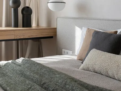 A serene minimalist bedroom featuring grey and neutral tones with a textured blanket and pillows.