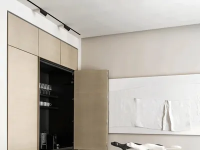 A modern minimalist kitchen with a wooden cabinet and island, white countertop, and black stools.