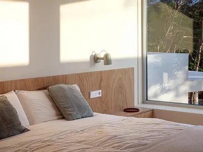Modern minimalist bedroom with wooden accents featuring a bed with white bedding, grey pillows, and a wooden headboard under