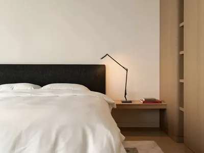 A modern minimalist bedroom featuring a bed with white bedding, a black headboard, and a wooden nightstand with a black lamp