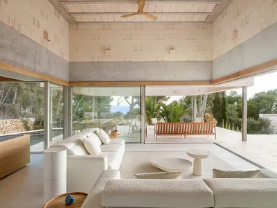 Modern minimalist living room featuring concrete walls, wooden furniture, a white cotton sofa, and a glass coffee table.