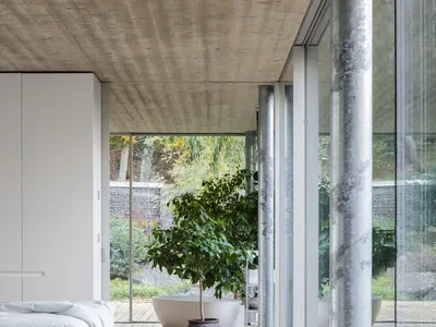 A minimalist bedroom featuring a concrete ceiling and wooden floor, with a large window showcasing outdoor greenery.
