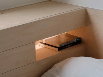 A minimalistic bedroom featuring a built-in nightstand made of light-colored wood.
