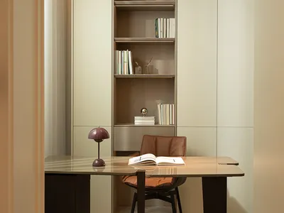 A modern home office with a sleek desk, leather chair, wooden bookshelf, and minimalist interior design.