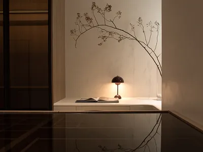 A minimalist bedroom with a wooden table, a lamp, and an open book.