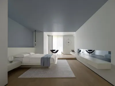A modern minimalist bedroom with concrete surfaces, featuring a low bed platform, floating nightstands, and a sleek, contempo