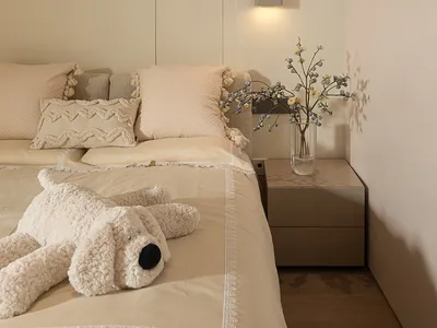 A minimalist bedroom decorated with neutral-toned textiles, featuring a cozy stuffed animal on the bed and a vase of flowers