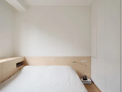 Minimalist bedroom with a white platform bed, wood floor, and white walls.