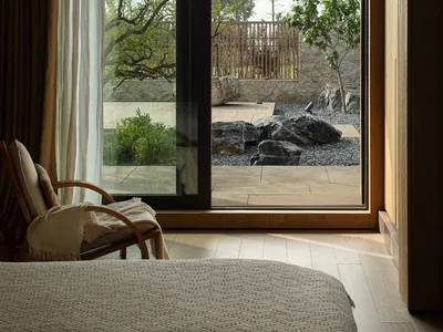 A modern minimalist bedroom with a large glass window overlooking a serene outdoor garden.