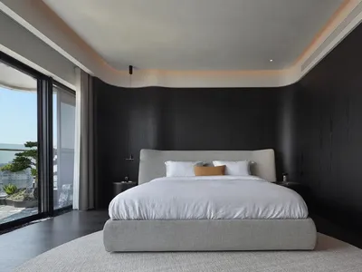 A modern minimalist bedroom featuring black walls, a white upholstered bed with a low-profile headboard, and a large window p