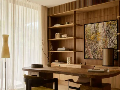 A modern home office featuring a wooden desk and shelving unit with decorative items and a large artwork.