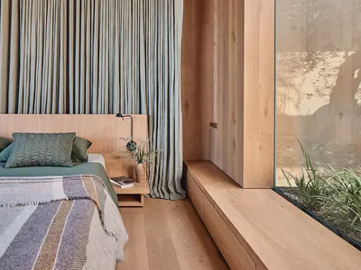 Modern minimalist bedroom with wooden furniture and green accent pillows.