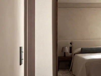A minimalist bedroom with a bed covered in neutral-toned textiles and a mirror on the wall.