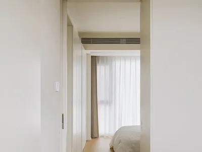 Minimalist bedroom featuring white walls and floor, with a bed and curtains.