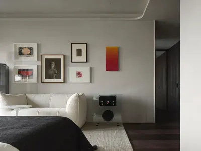 Neutral-colored bedroom with minimalist design, featuring a white sofa and a single orange-red abstract painting.