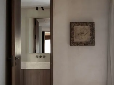 Minimalist bedroom with neutral tones, featuring a bed, a door leading to an en-suite bathroom, and a framed artwork on the w