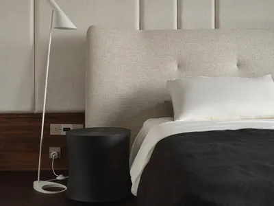 A minimalist bedroom with a white upholstered bed, white bedding, and a plain fabric headboard.