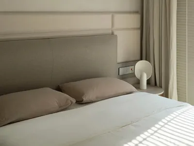 A minimalist bedroom with a bed, pillows, and a side table with a lamp.