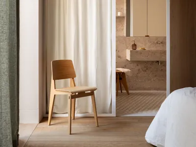 A minimalist bedroom featuring wooden furniture and a white bed.