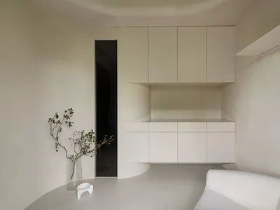 A minimalist kitchen with concrete finishes, featuring sleek white cabinets and a white, textured sofa.