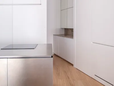 Modern minimalist kitchen with white surfaces and stainless steel appliances.