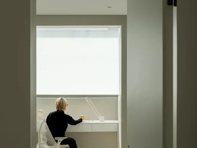 A modern home office desk setup with a person sitting at it, illuminated by a lamp.