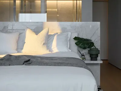 A minimalist bedroom featuring a marble headboard and a green plant on the nightstand.