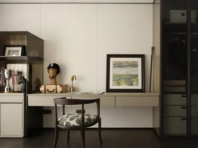 A minimalist home office space featuring a wooden desk, glass cabinet, and metal chair, with a framed abstract painting and v