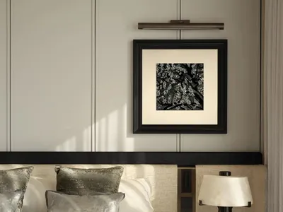 A modern minimalist bedroom with grey fabric bedding, metallic grey pillows, and a matte black table lamp with a white shade.