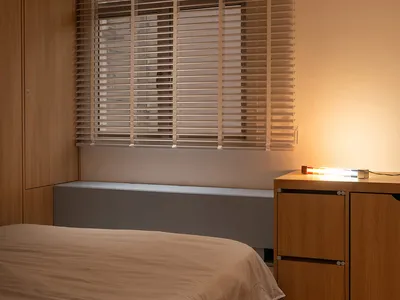 A minimalist bedroom featuring wooden blinds and a bed covered with a beige duvet.