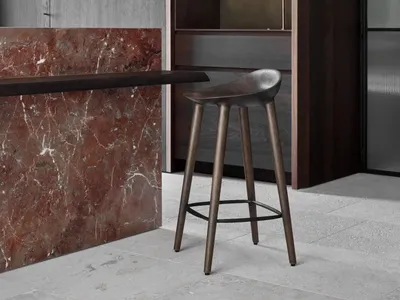 A modern kitchen with a marble countertop, wooden stools, and metallic accents.