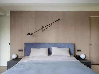A modern minimalist bedroom featuring a bed with a blue upholstered headboard, white bedding, and a sleek black adjustable re