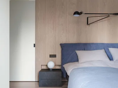 A modern minimalist bedroom featuring wooden paneling, a blue upholstered bed, and a sleek black floor lamp.