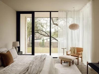 A minimalist bedroom with natural fibers, featuring a bed, side table, armchair, and footstool.