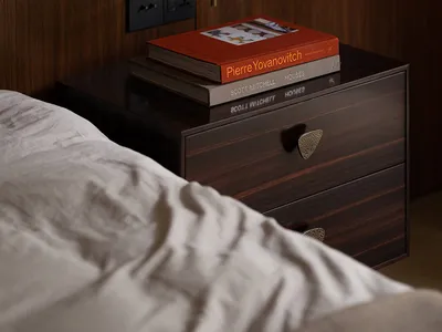 A minimalist bedroom featuring a wooden nightstand with books and a lamp.
