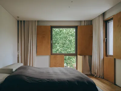 Modern minimalist bedroom with wood cabinets, fabric curtains, and a glass window.