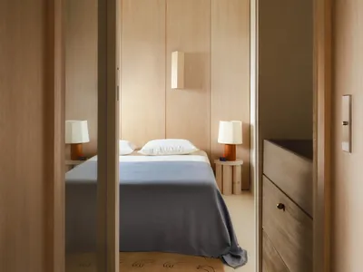 A minimalist bedroom with wooden walls and blue textiles, featuring a single bed, nightstands, and a small rug.