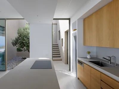 Modern minimalist residential kitchen featuring a sleek black countertop with a built-in stove, wooden cabinets, and a view o