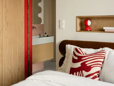 Contemporary bedroom featuring light wooden cabinets, ceramic tiles, and a plush bed with red and white decorative pillows.