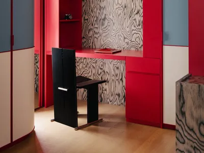 A modern home office with red walls, a black chair, and a wooden textured wall.