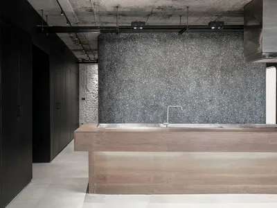 A modern, minimalist kitchen featuring a concrete wall and a wooden countertop with a stainless steel sink and faucet.