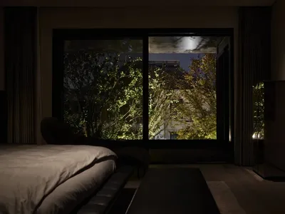 A modern bedroom featuring glass walls with a view of the outdoors at dusk.