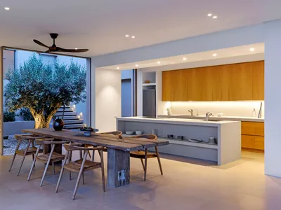 A modern kitchen with a wooden table and chairs, featuring a large tree in the background.